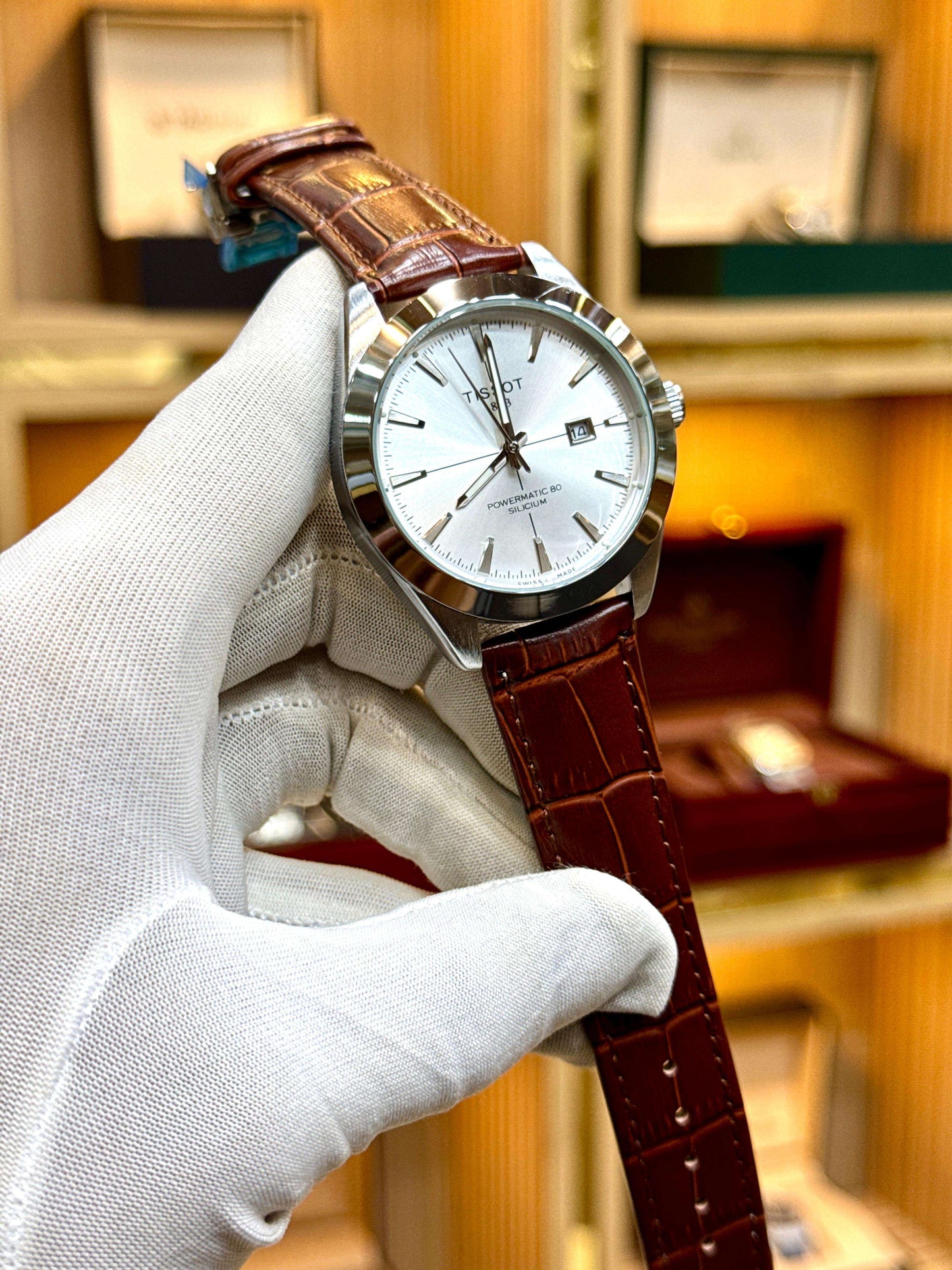 Watch with brown leather strap held by a gloved hand against a blurred background